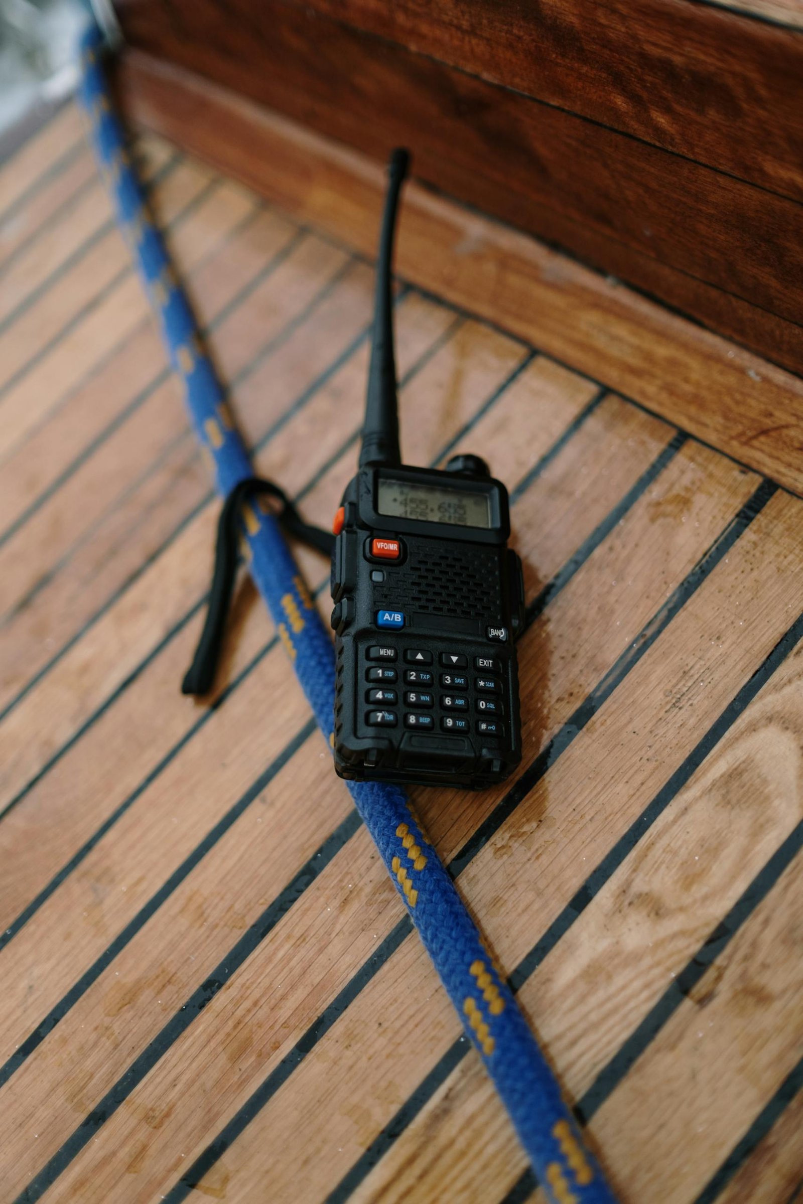 A two-way radio placed on a wooden surface next to a blue rope, possibly on a boat deck.